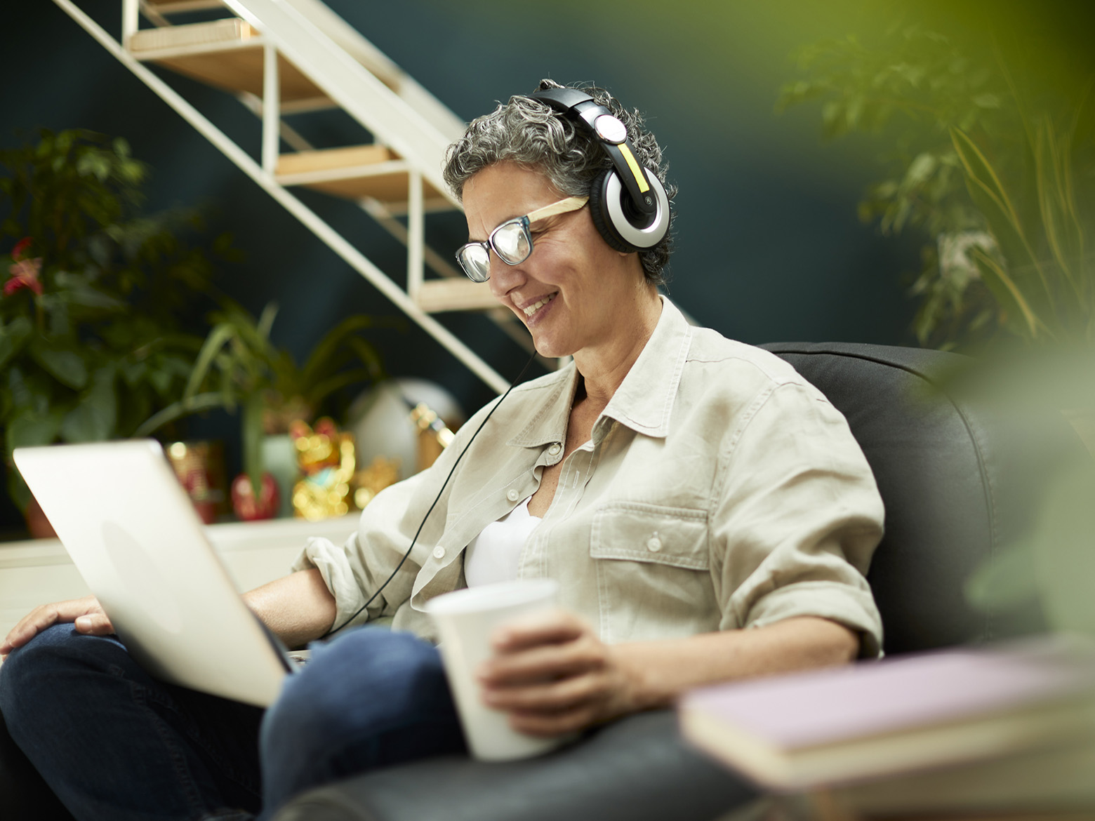 A woman sits with headphones on plugged into her laptop