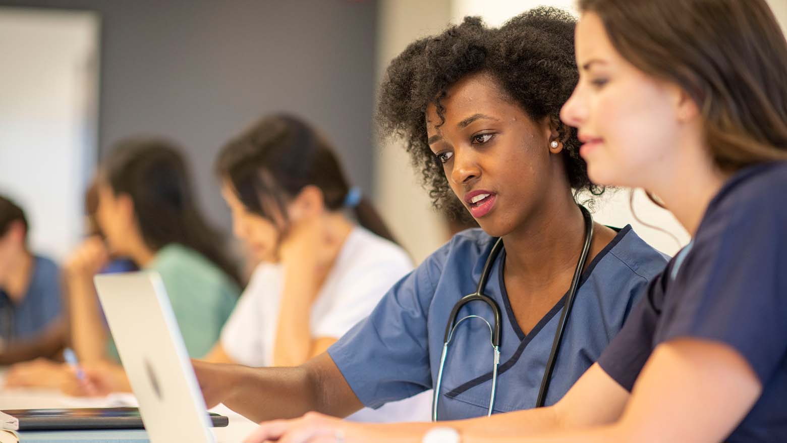 Two female medical students converse while looking at a laptop screen