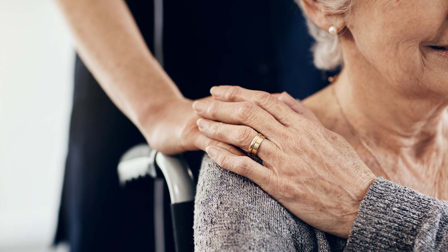 A caregiver holds the hand of an elderly woman in a wheelchair