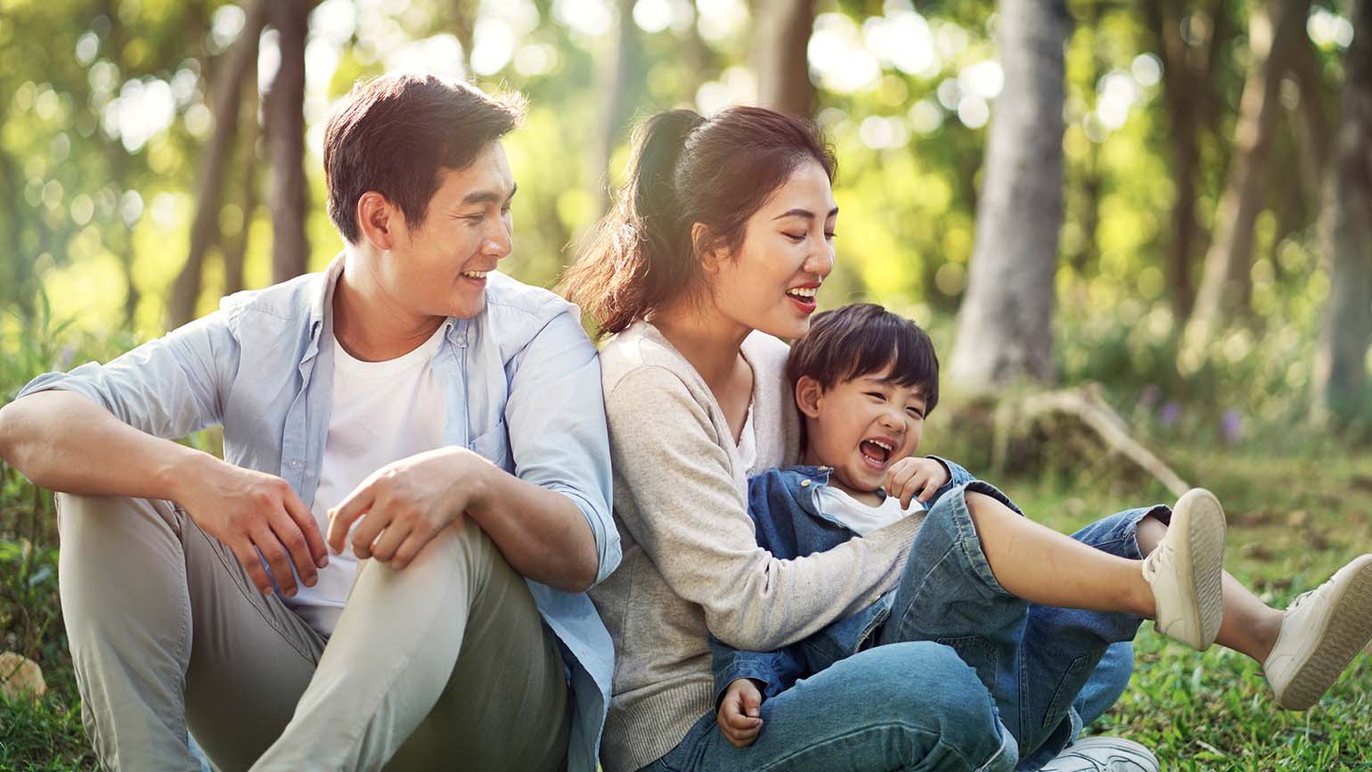 A mother and father playing with their kid in a park.