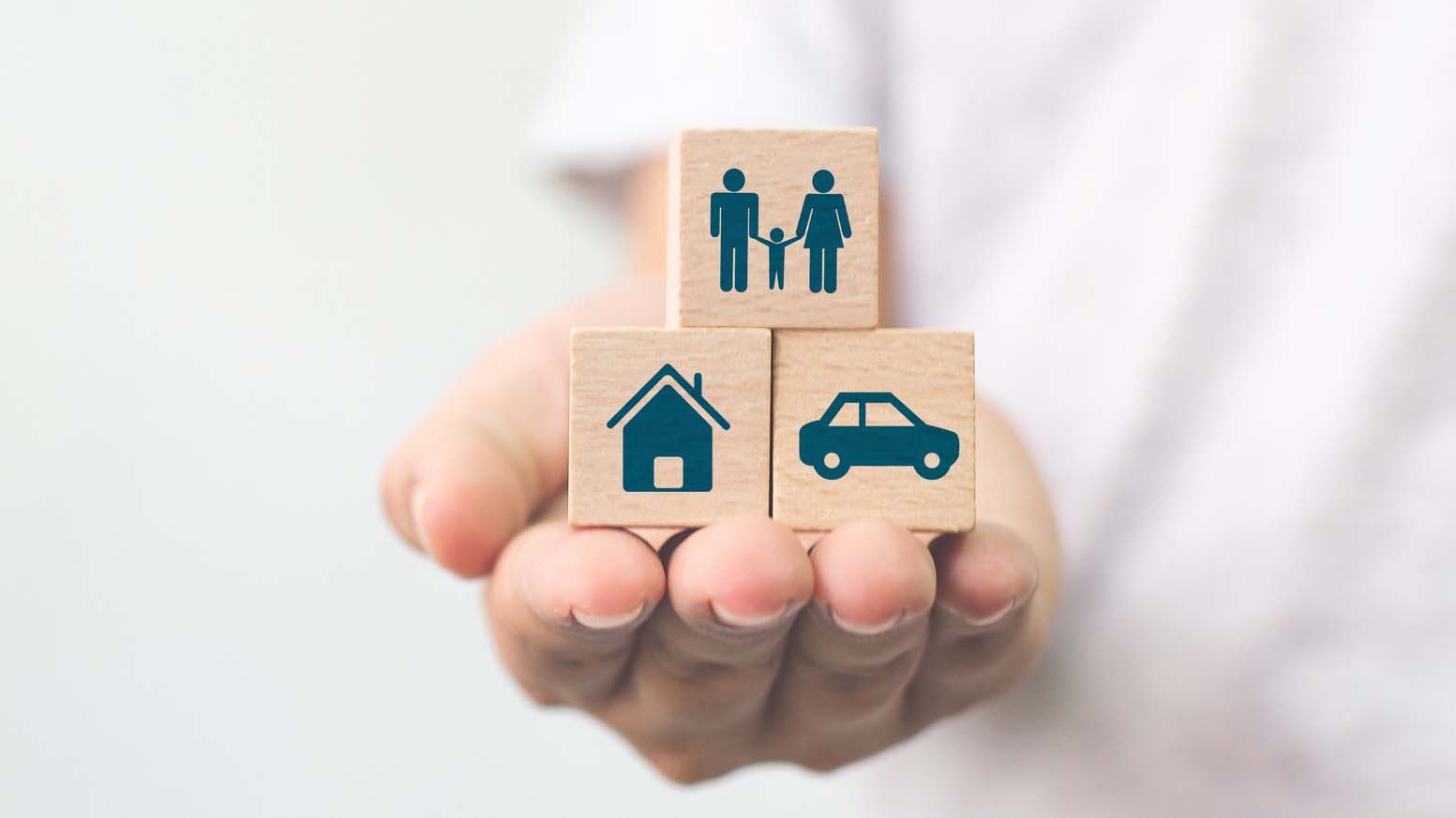A hand holding out three blocks with symbols depicting a house, a car, and a family