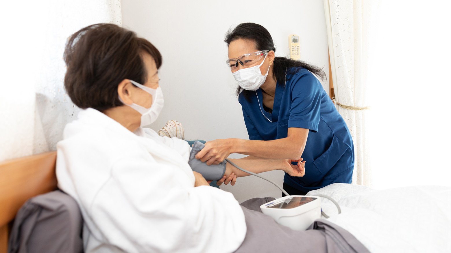 A patient sits in bed while her blood pressure is taken by a nurse