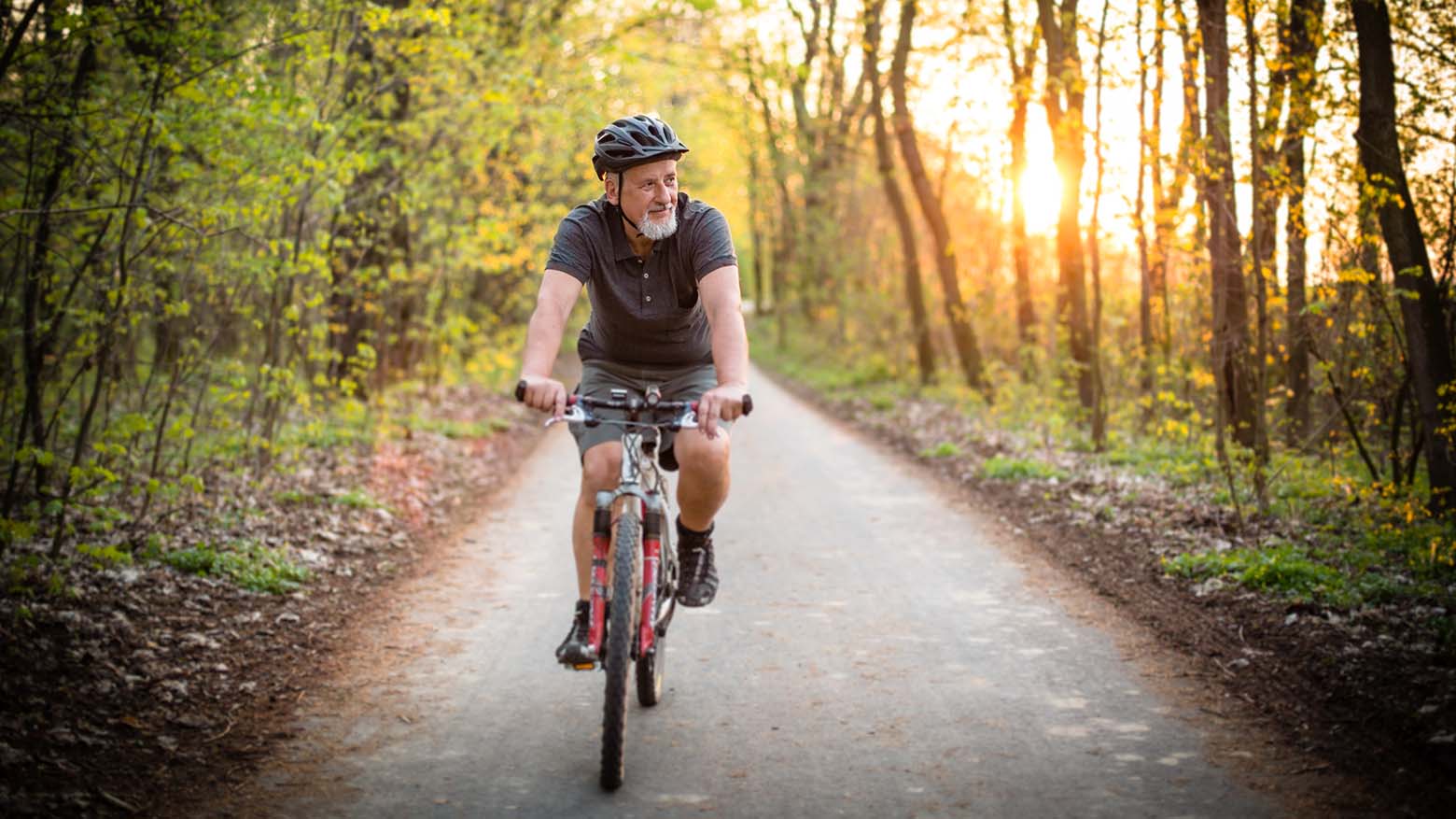 An older man rides a bicycle through a nature trail