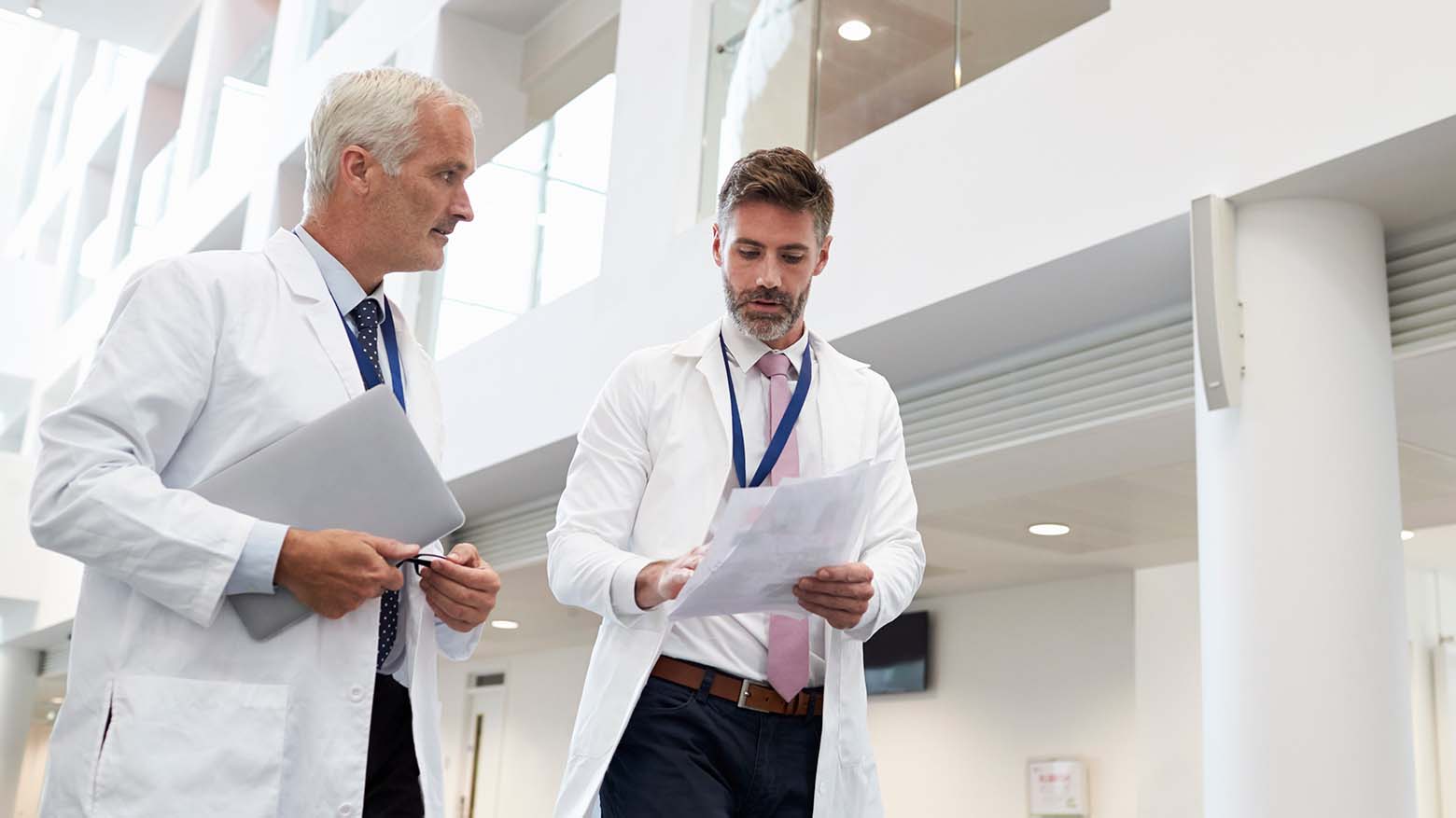 A male doctor discusses paperwork while walking with an older male doctor