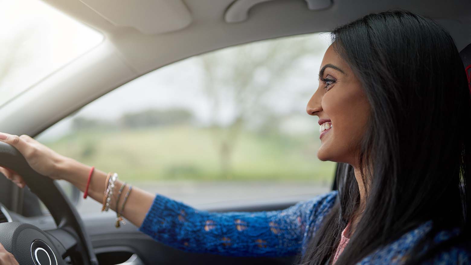 A woman smiles while driving a car
