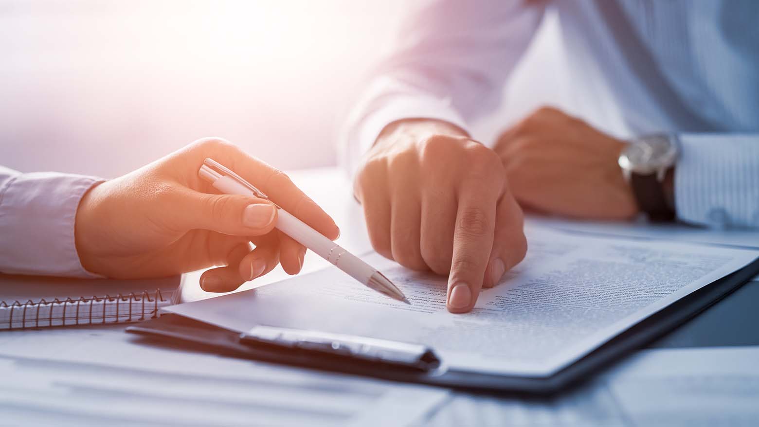 Two sets of hands point at lines of text on a clipboard