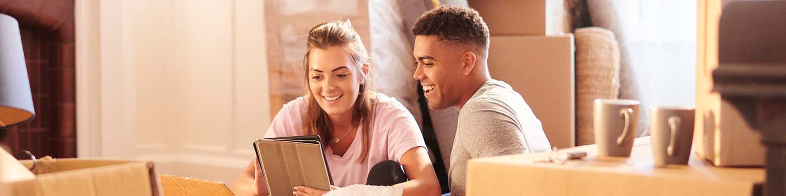 A young couple sits on the floor of their living room to unpack moving boxes