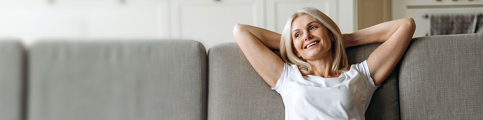 A woman leans back while sitting on a couch with her arms crossed behind her head