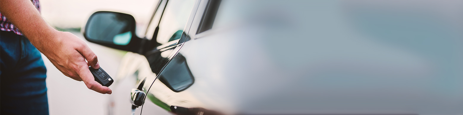 A man holds his car key fob close to his car door to unlock it