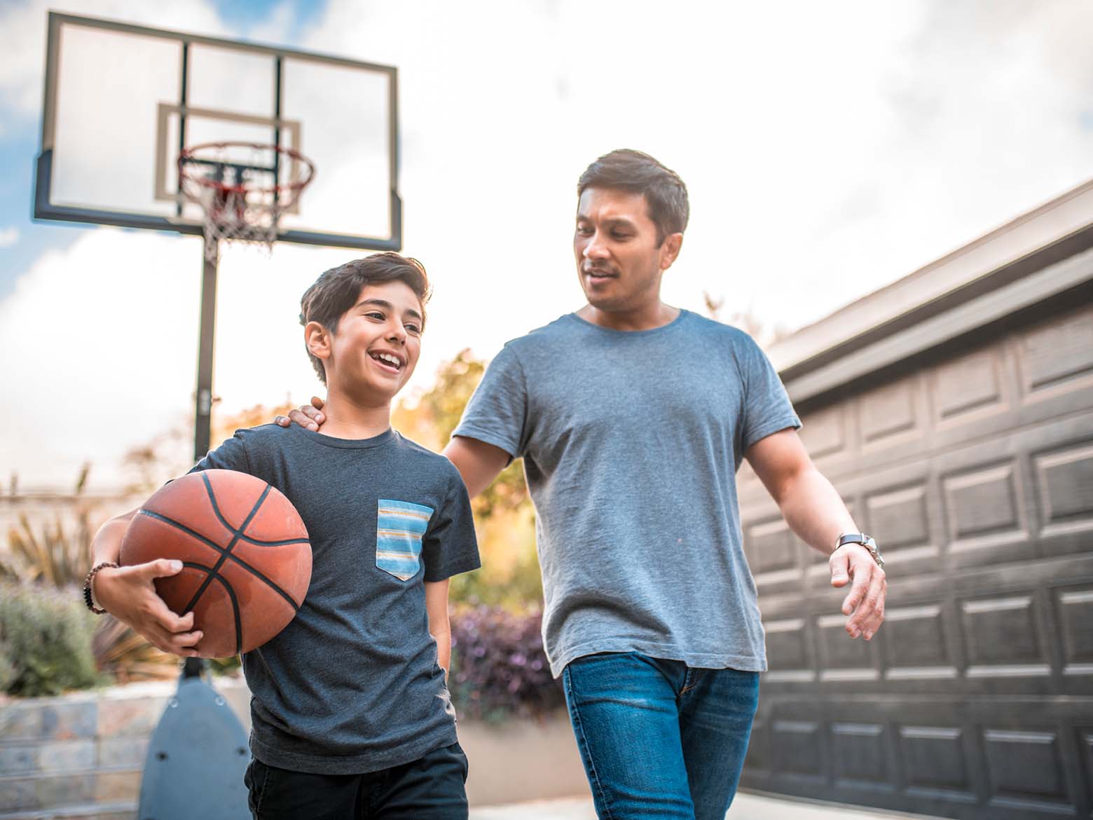 A boy holds a basketball while walking away from a basketball net with his father