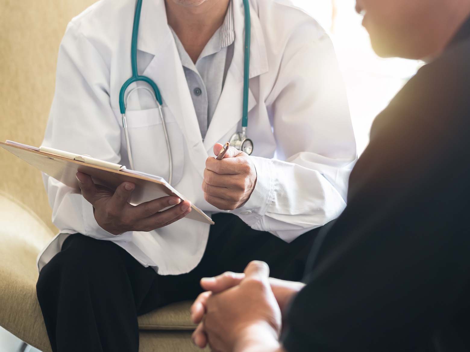 A doctor holds out a clipboard and pen to a patient