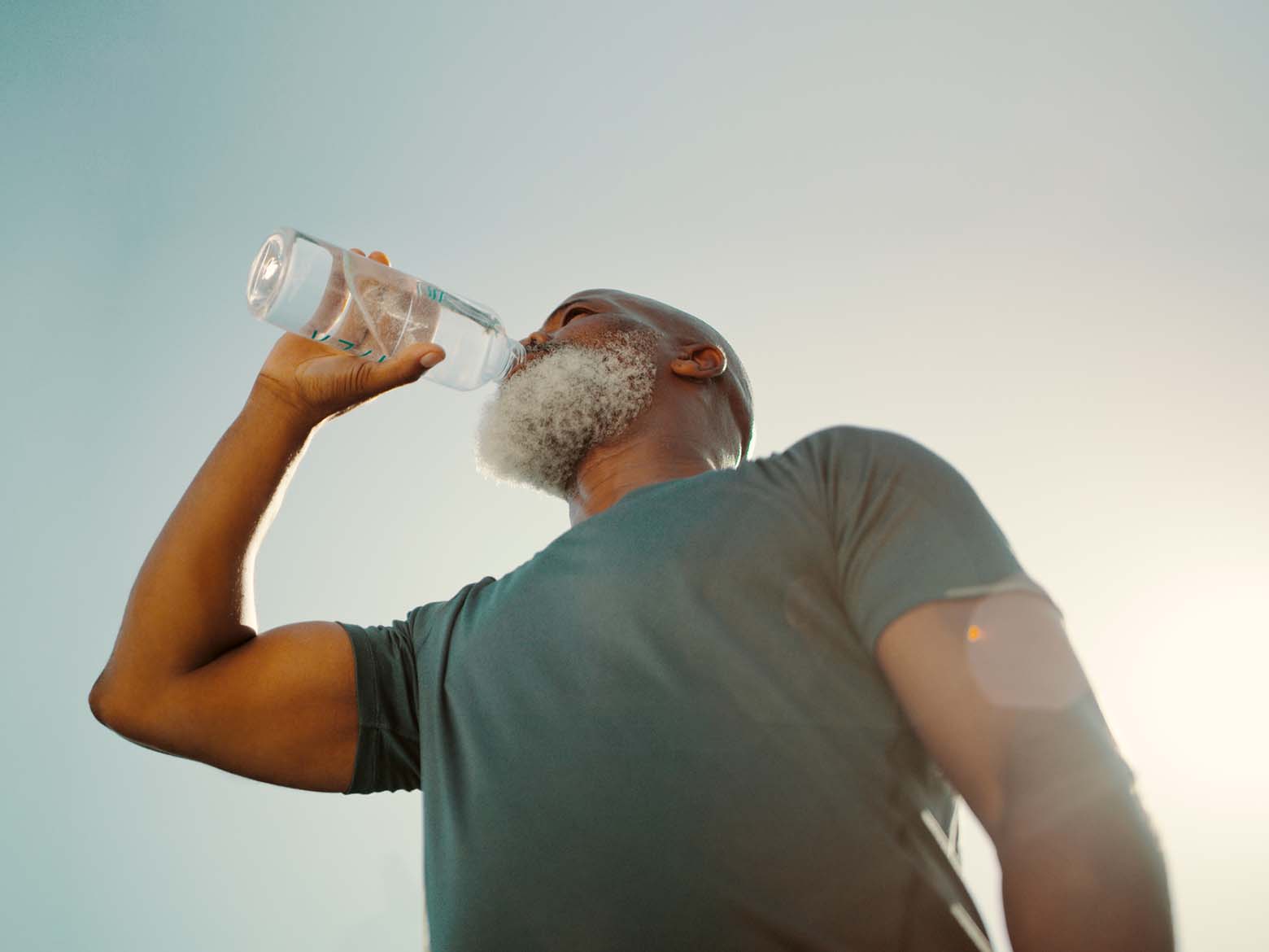 A man on a walk stops to take a drink of water from a bottle