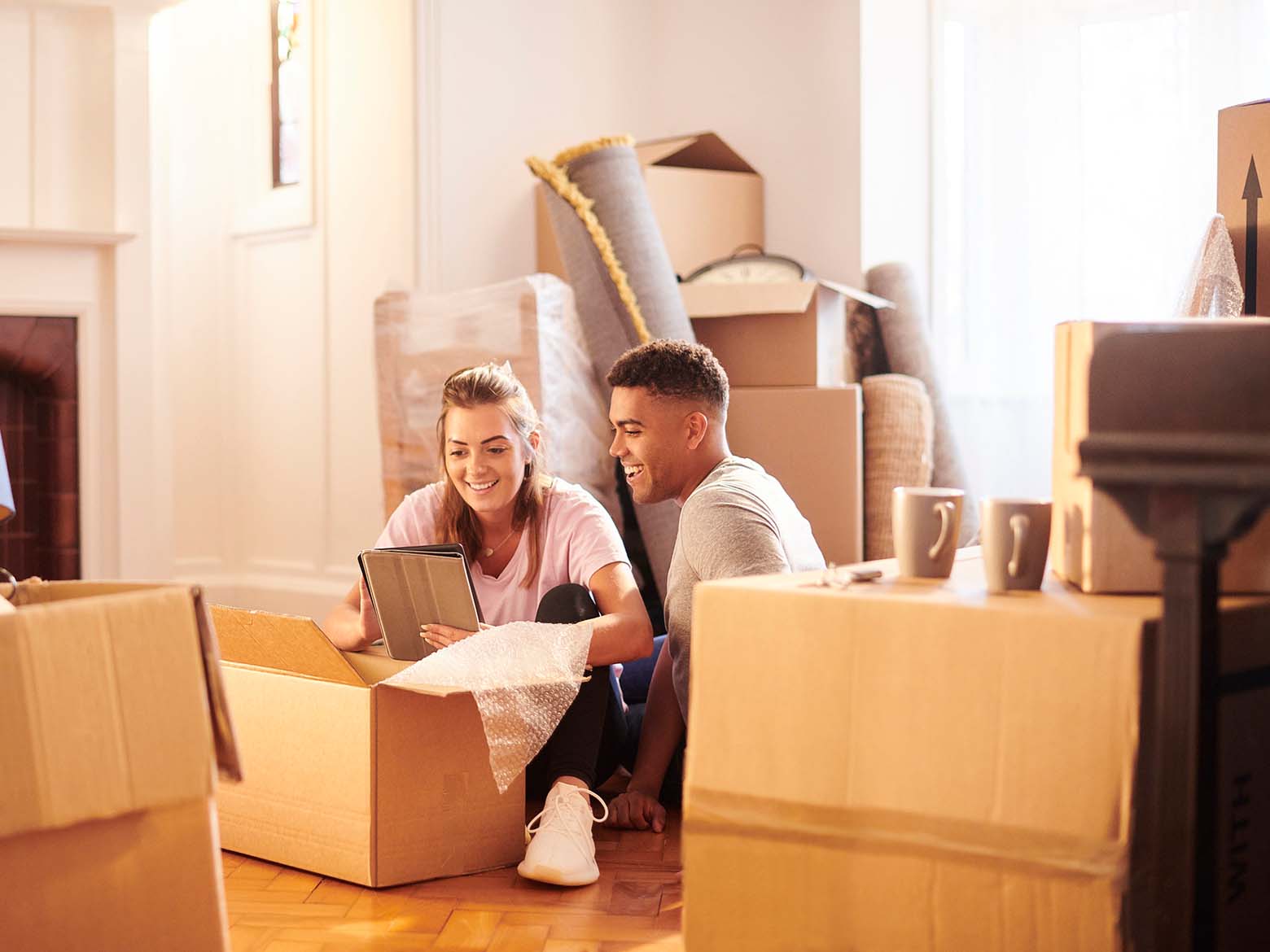 A young couple sits on the floor of their living room to unpack moving boxes