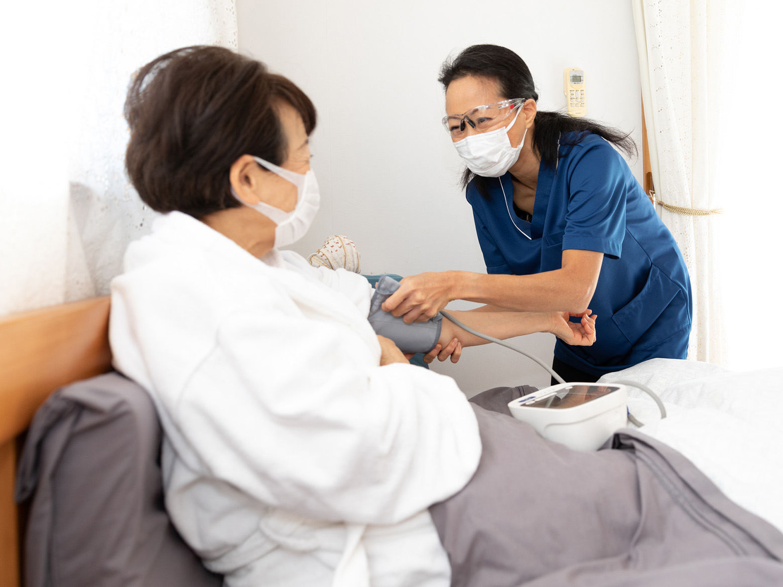 A patient sits in bed while her blood pressure is taken by a nurse