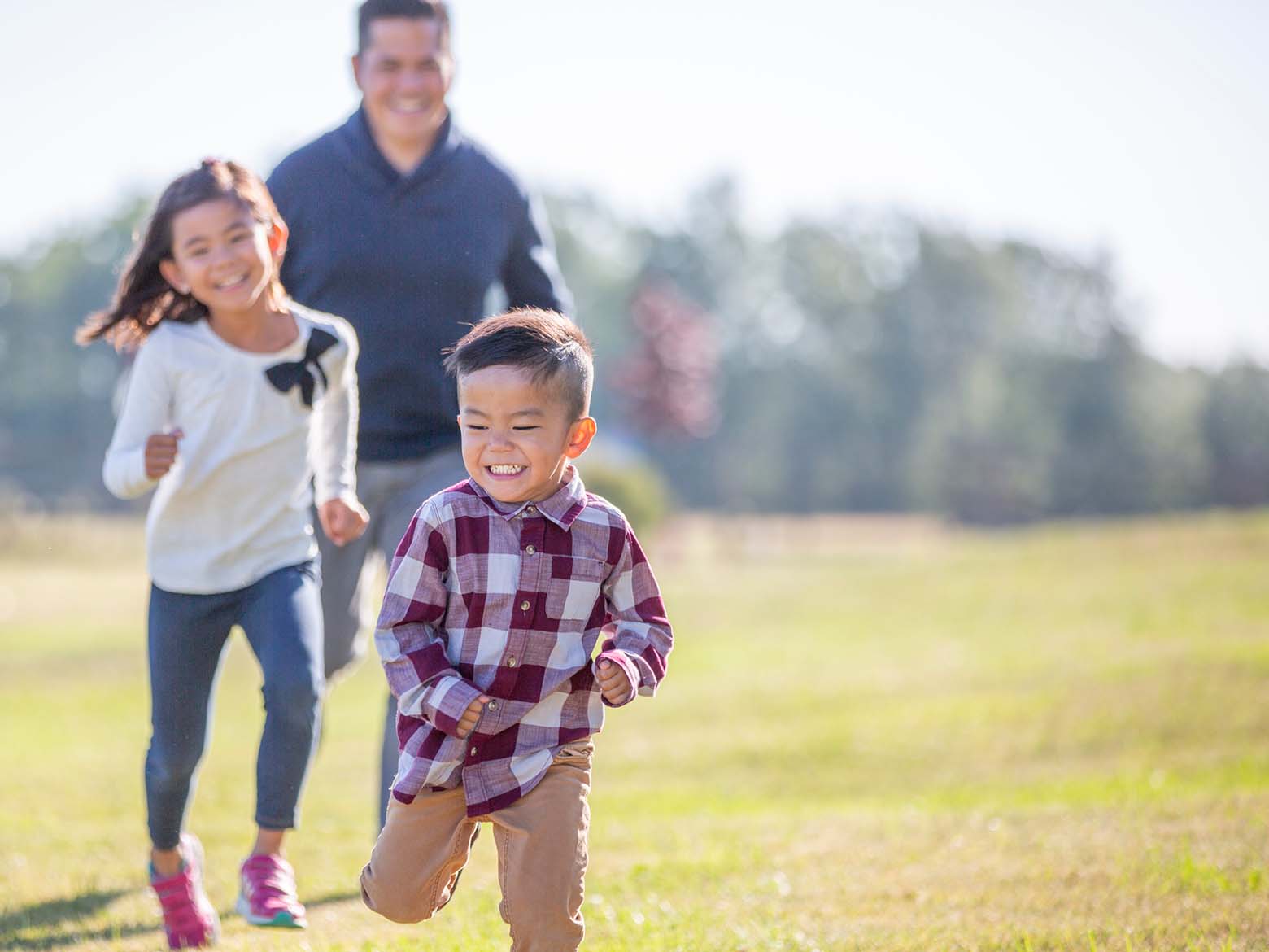 A man and his two young children run in a field while laughing