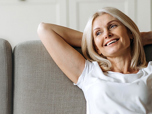 A woman leans back while sitting on a couch with her arms crossed behind her head