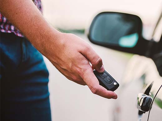 A man holds his car key fob close to his car door to unlock it