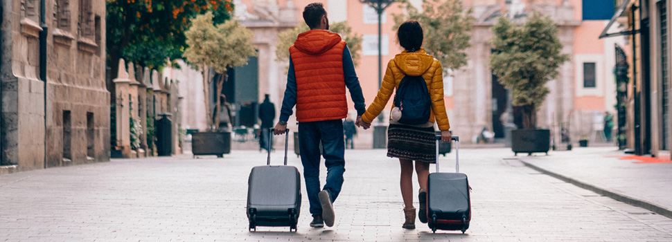 A couple walk along a street while rolling their luggage