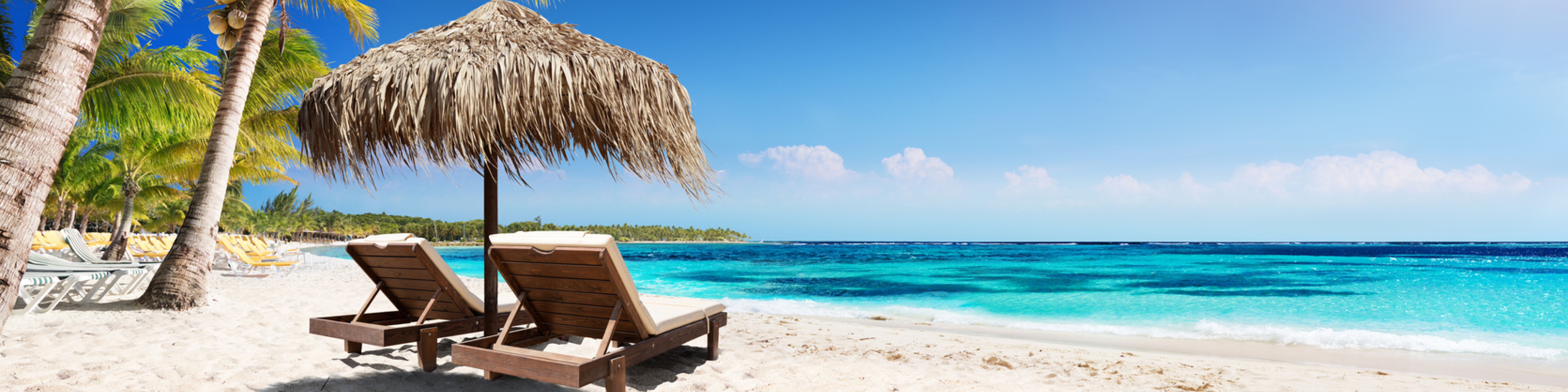 Two lounge chairs under an umbrella on the sand at a beach